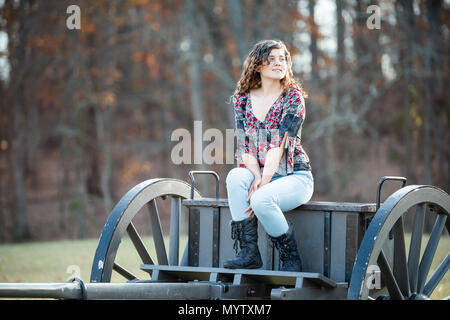 Young happy woman smiling sitting on old cannon carriage in Manassas National Battlefield Park in Virginia where Bull Run battle was fought, sunlight Stock Photo