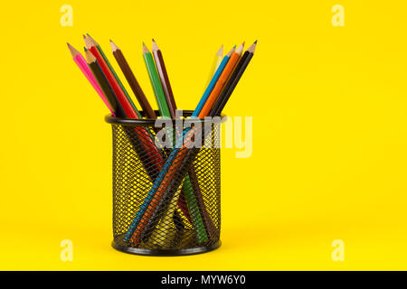 Colored wooden pencil in black metal basket isolated on yellow background. Education and Art concept
