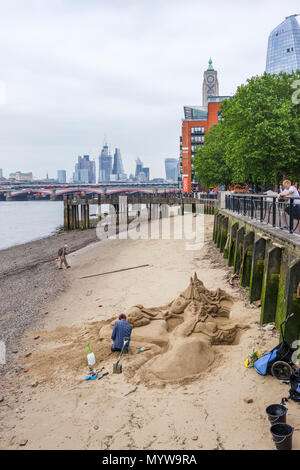 Sand sculptor working on a sculpture on a beach at low tide on the River Thames, South Bank Embankment riverside walkvnear Oxo Tower Wharf, London SE1 Stock Photo