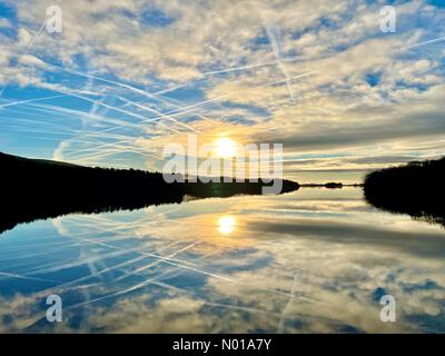 UK Weather: Sunny morning at Rivington. Cold sunny winter morning with sun and clouds reflected in Rivington reservoir near Chorley in Lancashire Stock Photo