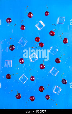 Cherry and ice cube pattern on a bright blue background. A cocktail concept for a hot summer day
