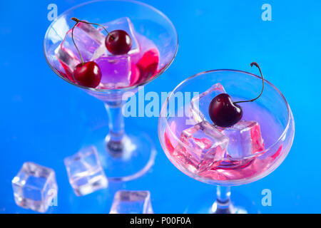 Cherry drink in cocktail glasses with ice cubes on a blue background. Refreshing cold drink with copy space. Summer beverage concept Stock Photo