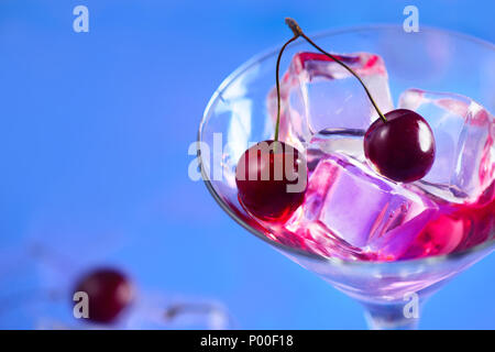 Cherry cocktail close-up. Martini glass with ice cubes and cherries on a bright blue background with copy space. Hot summer day refreshment concept