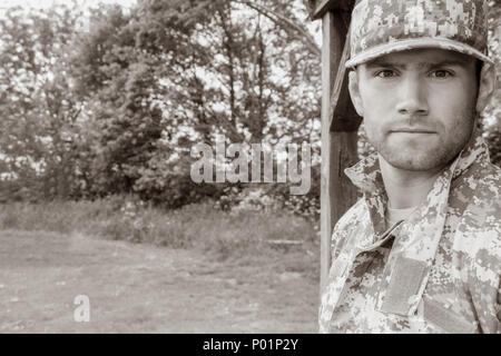 Muscular military man in army fatigues and cap stands to attention while guarding army base Stock Photo
