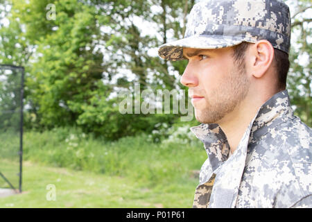 Muscular military man in army fatigues and cap stands to attention while guarding army base Stock Photo