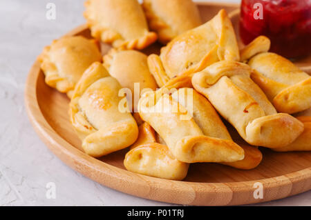 Two types of empanadas on a wooden plate with ketchup. White stone background. Stock Photo