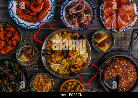 Typical spanish tapas concept. Concept include slices jamon, bowls with olives,  anchovies, spicy potatoes, mashed chickpeas, shrimp, calamari, manche Stock Photo