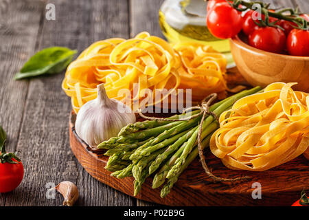 Products for cooking - fresh asparagus, pasta, tomatoes, garlic, olive oil on the old wooden background. Stock Photo