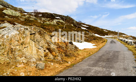 Small and narrow country road in the mountains. Snow and ice is melting in the sunshine. Location above the lake Kjelavatn in Telemark, Norway. Stock Photo