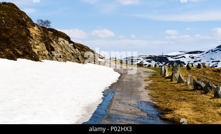 Small and narrow country road in the mountains. Snow and ice is melting in the sunshine. Location above the lake Kjelavatn in Telemark, Norway. Stock Photo