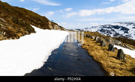 Small and narrow country road in the mountains. Snow and ice is melting in the sunshine. Location above the lake Kjelavatn in Telemark, Norway. Stock Photo