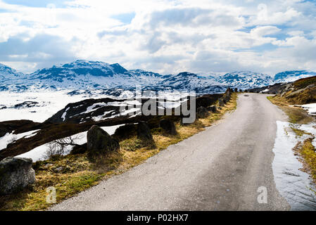 Small and narrow country road in the mountains. Snow and ice is melting in the sunshine. Location above the lake Kjelavatn in Telemark, Norway. Stock Photo