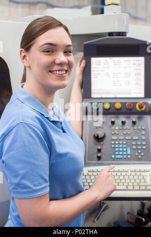 Portrait Of Female Apprentice Engineer Operating CNC Machine In Factory Stock Photo