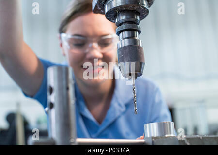 Female Apprentice Using Drill In Factory Stock Photo