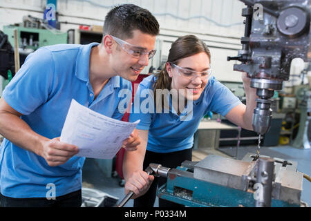 Engineer Instructing Female Apprentice On Use Of Drill Stock Photo