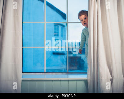 A cute little boy is hiding behind the curtain in the morning Stock Photo