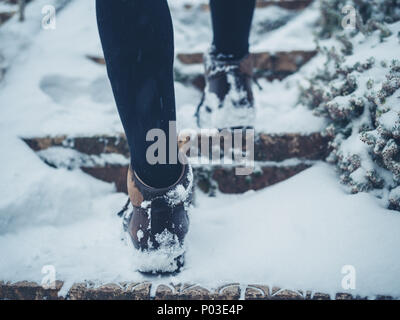 The feet of a young woman wearing boots walking up some steps in the snow Stock Photo