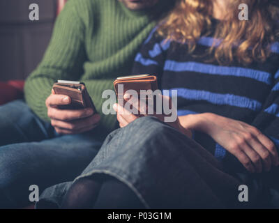 A man and a woman are sitting on a sofa using their smart phones Stock Photo