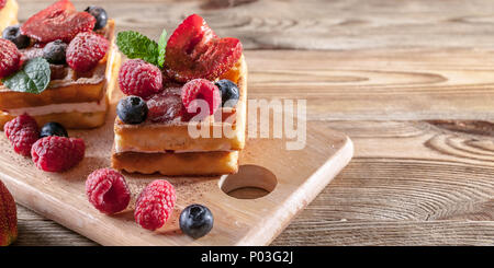 Belgian waffles with strawberry jam, fresh strawberries, raspberries, blueberries and chocolate chips on a wooden table. Homemade baking. Delicious br Stock Photo