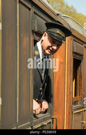 Portrait close up of gentleman ticket inspector on Severn Valley Railway, leaning out of carriage window in the sunshine, ready to greet passengers. Stock Photo