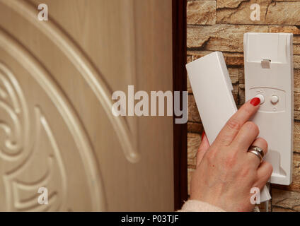 In the hallway hangs an intercom. The female hand presses a button to open the door. Stock Photo