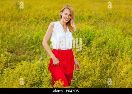 Smiling girl stands in a field of yellow flowers and poses in front of a photo camera