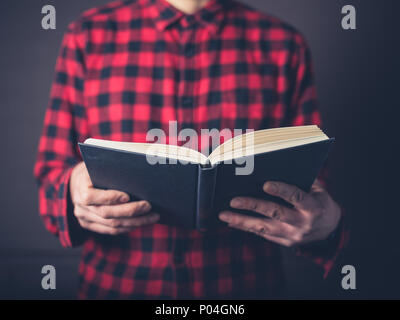 A young man wearing a flannel shirt is reading a book Stock Photo