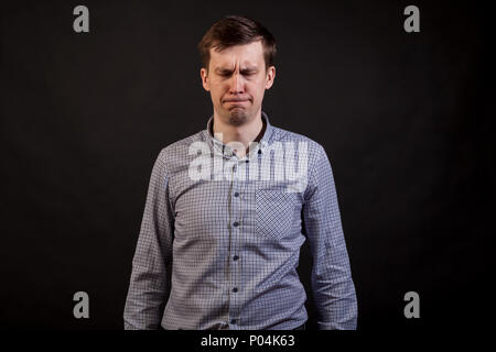 A dark haired white man with a sad and boring face closed eyes in a plaid shirt and jeans on a black isolated background Stock Photo