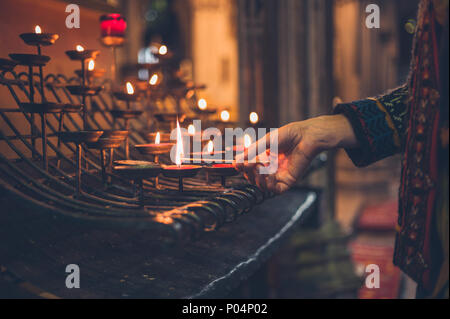 The hand of a young woman is lighting a votive candle in a church Stock Photo