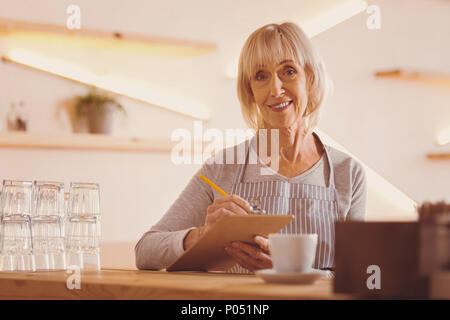 Cheerful woman checking customers orders in her notes Stock Photo