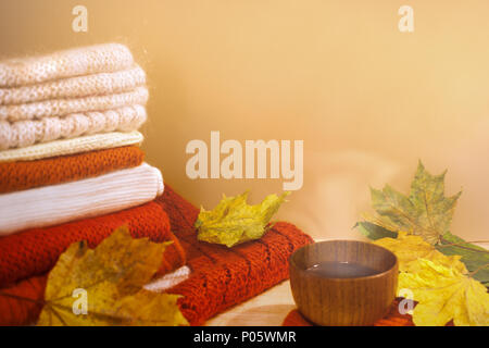 Warm knitwears, multicolor maple leaves and wooden cup of hot tea on light background with copy space. Stock Photo