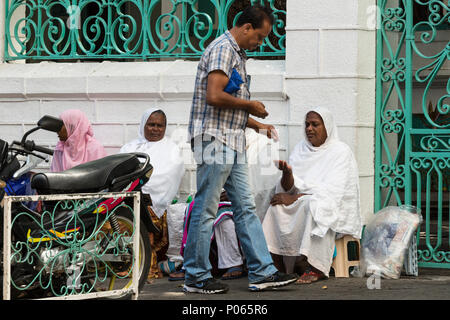 A passerby giving money to one of a group of women sitting on the street waiting for alms outside Jummah Mosque on a Friday, Port Louis,  Mauritius Stock Photo