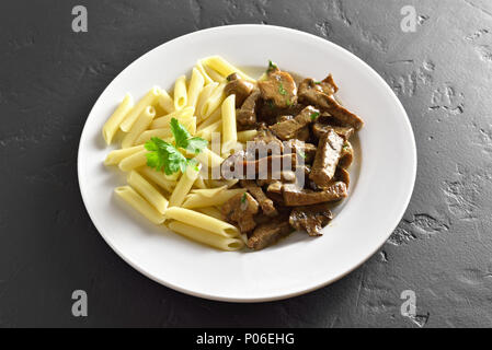 Beef stroganoff with pasta on plate on black stone background. Stock Photo