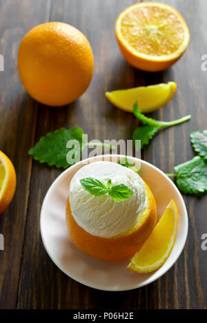 Tasty orange ice cream in fruit on wooden table. Cold summer dessert. Stock Photo