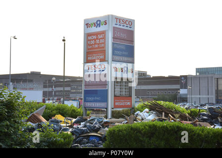 Fly tipping rubbish is left in front of the shop signs including Tesco Direct and The Toys R Us both now closed stores, on the North Circular, near th Stock Photo