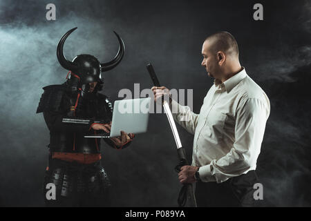 man with katana standing in fornt of samurai while he using laptop Stock Photo