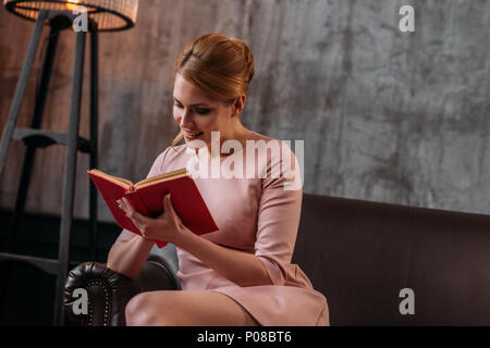 concentrated young woman reading book on couch in loft interior Stock Photo
