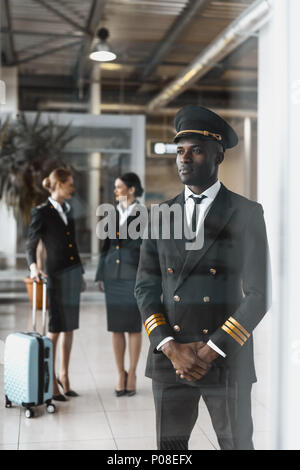handsome young pilot in airport with stewardesses before flight Stock Photo