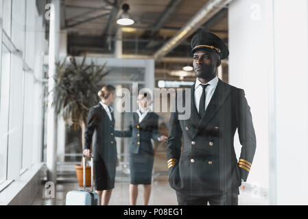thoughtful young pilot in airport with stewardesses before flight Stock Photo