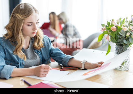 beautiful magazine editor drawing sketches in modern office, coworkers sitting behind Stock Photo