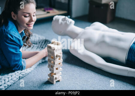 beautiful woman lying near mannequin and blocks wood game on floor at home, loneliness concept Stock Photo