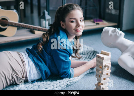 beautiful woman lying near mannequin and blocks wood game on floor at home, loneliness concept Stock Photo