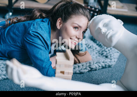 beautiful woman lying near mannequin and blocks wood game on floor at home, loneliness concept Stock Photo