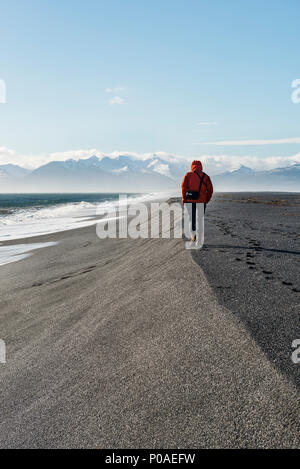 Man walking by the sea in the black sandy beach, lava beach, snow-capped mountains, Hvalnes Nature Reserve, South Iceland Stock Photo
