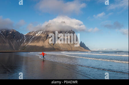Man runs in a good mood on a black sandy beach, mountains Klifatindur, Eystrahorn and Kambhorn, headland Stokksnes Stock Photo