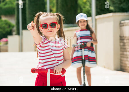 Preschooler girls riding scooter outdoors. Stock Photo