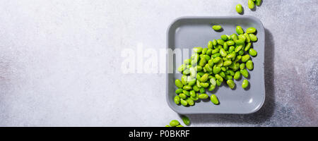 Green fresh soybeans on gray square plate on concrete background. Healthy food concept flat lay with coppy space. Top view. Banner. Stock Photo