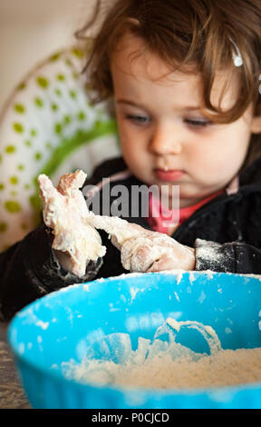 Little baby girl playing with dough on the high chair. Stock Photo