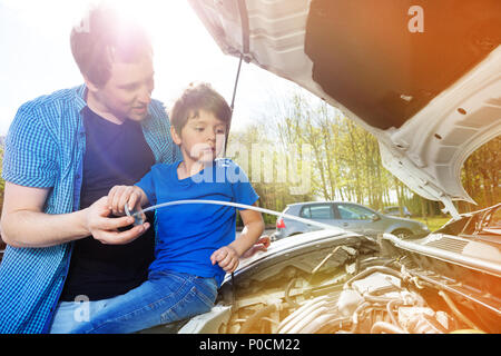 Father showing his 6 years old kid the oil level in car engine near the garage on sunny day Stock Photo