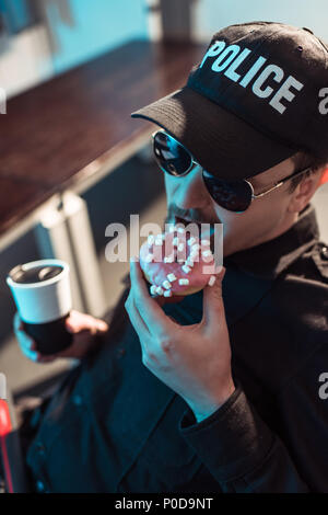 high angle view of prison guard eating doughnut and holding cup of coffee Stock Photo